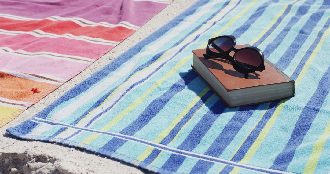 Sunglasses and book on striped beach towels at sandy coast - Free Images, Stock Photos and Pictures on Pikwizard.com