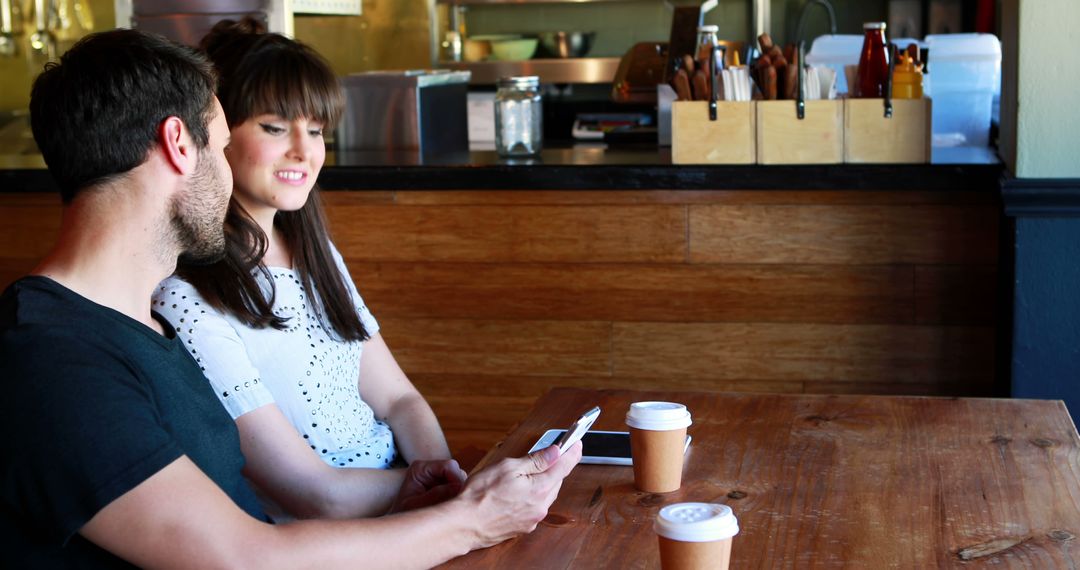 Smiling Couple in Cozy Café Enjoying Coffee and Phone Conversation