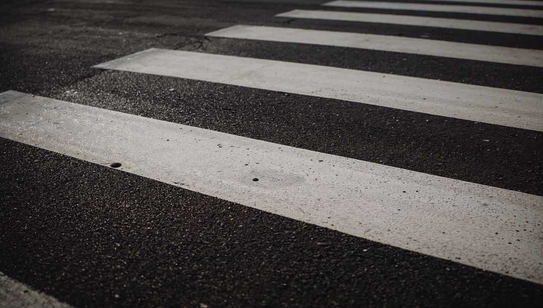 Close-up of weathered crosswalk stripes on asphalt showcasing diagonal perspective, texture