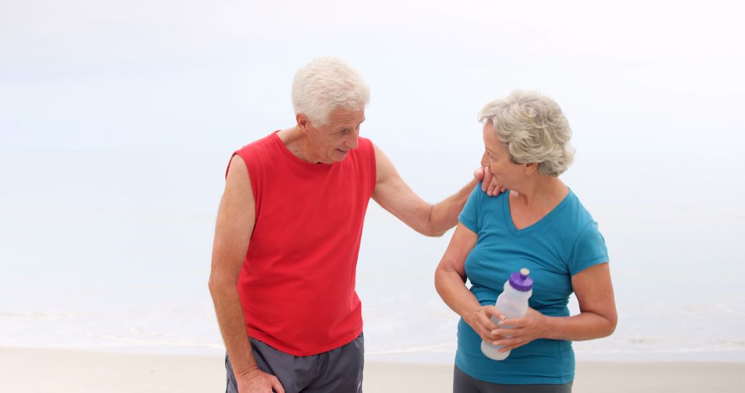 Senior Couple Enjoying a Walk on Beach Holding Water Bottle - Free Images, Stock Photos and Pictures on Pikwizard.com