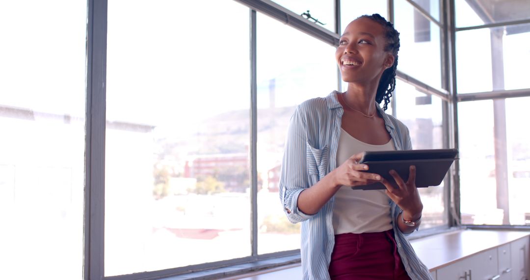 Smiling Woman Holding Tablet in Modern Office with Large Windows - Free Images, Stock Photos and Pictures on Pikwizard.com