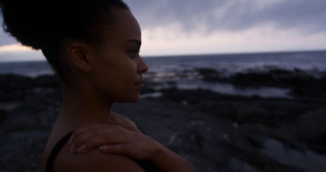 Contemplative Woman Standing on Rocky Shore at Dusk - Free Images, Stock Photos and Pictures on Pikwizard.com