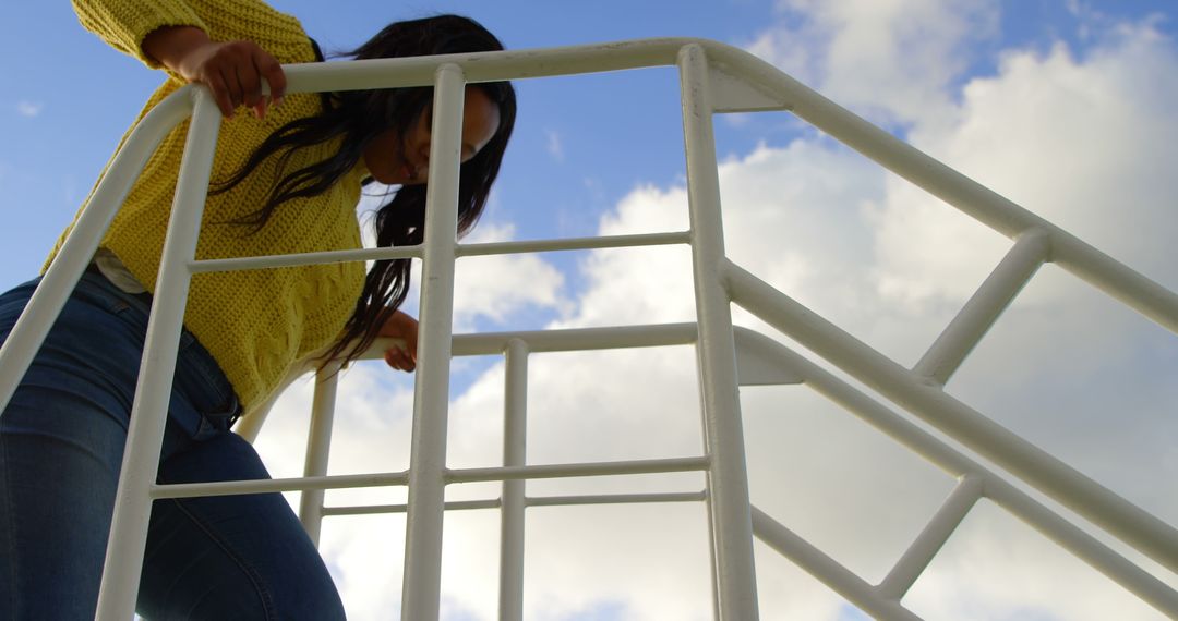 Woman Climbing Metal Stairs Against Blue Sky and Clouds - Free Images, Stock Photos and Pictures on Pikwizard.com