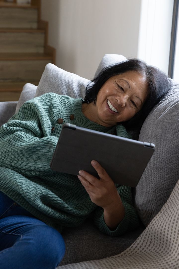 Senior Woman Smiling While Using Tablet on Comfortable Couch