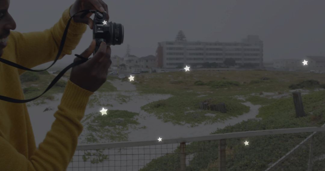 Man Using DSLR Camera Near Coastal Dunes on Overcast Day