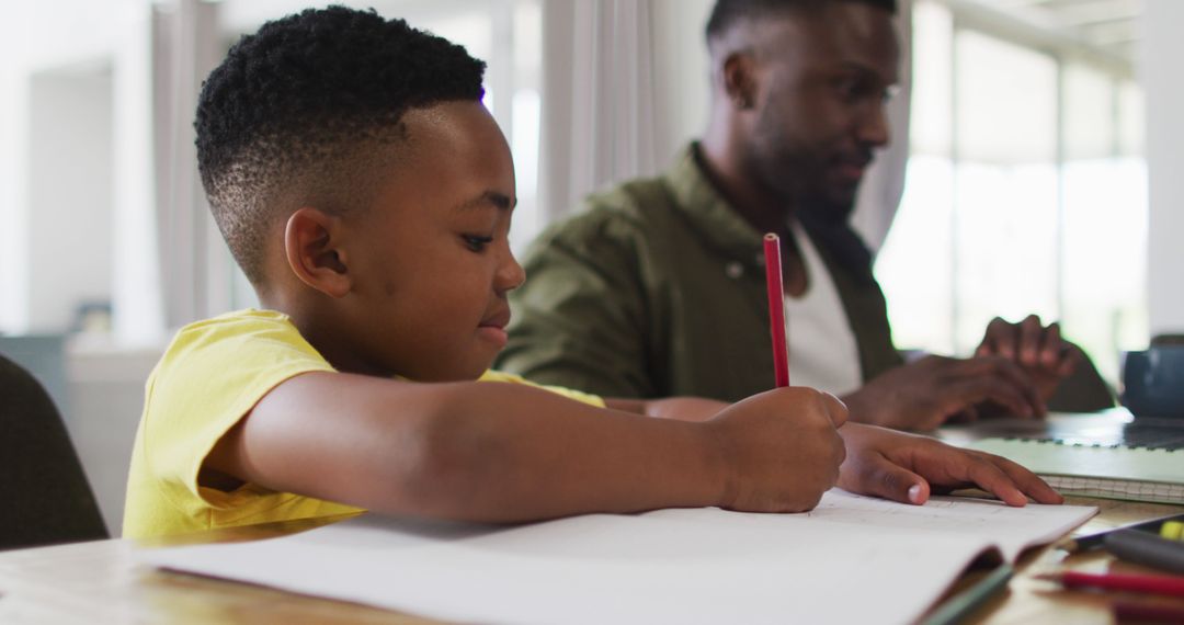 Young Boy Doing Homework with Focused Father Working in Background - Free Images, Stock Photos and Pictures on Pikwizard.com