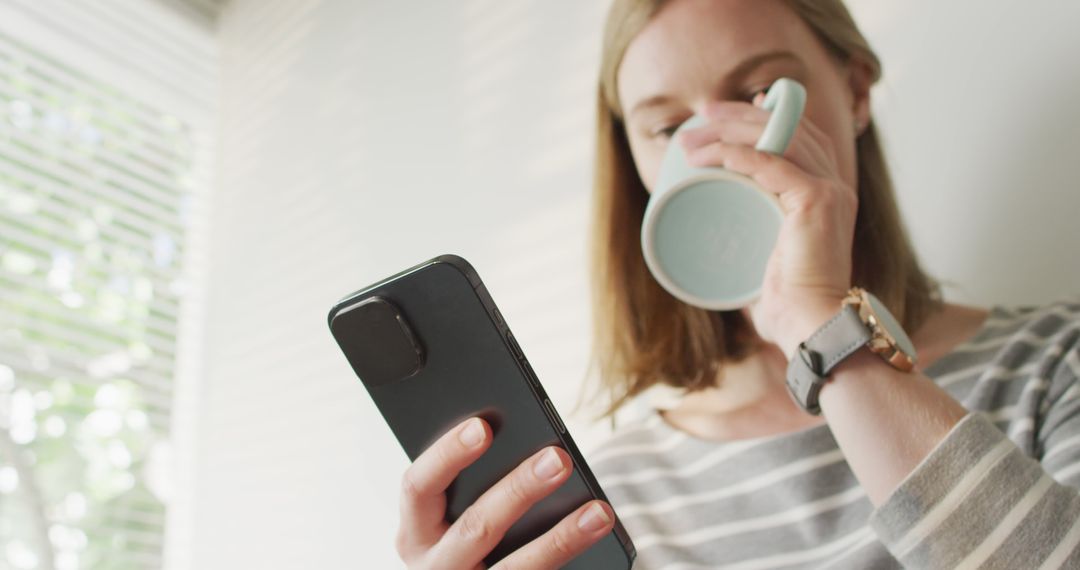 Young Woman Drinking Coffee While Using Smartphone Indoors - Free Images, Stock Photos and Pictures on Pikwizard.com