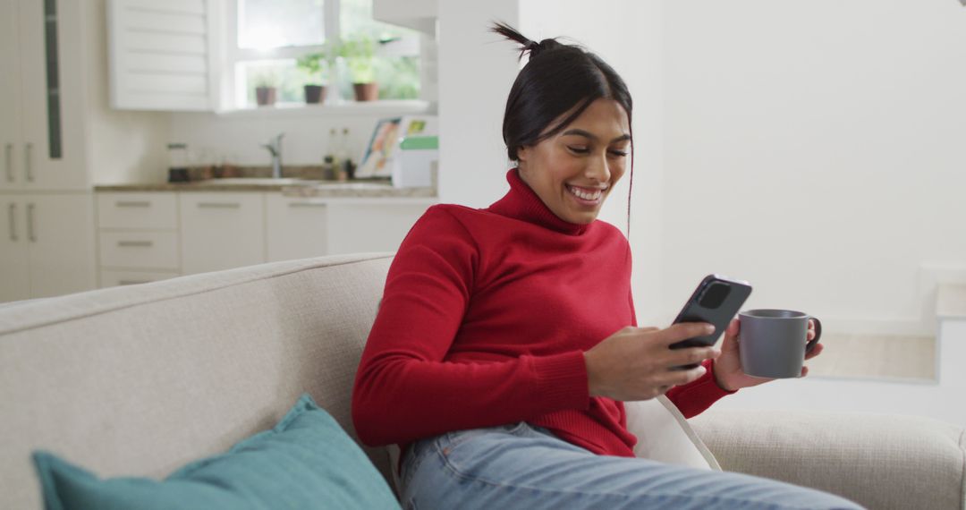 Image of happy biracial woman in hijab sitting on sofa and using smartphone - Free Images, Stock Photos and Pictures on Pikwizard.com