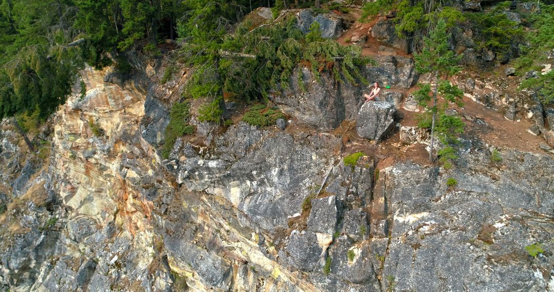 A person sits on the edge of a steep cliff surrounded by lush greenery, with copy space - Free Images, Stock Photos and Pictures on Pikwizard.com