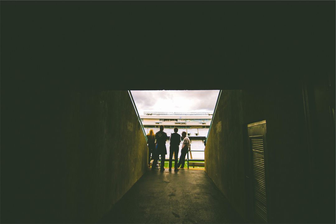 Silhouetted spectators standing at stadium tunnel entrance overlooking empty field