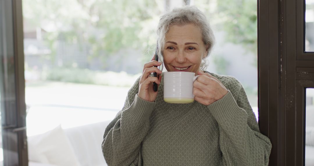 Senior Woman Drinking Coffee While Talking On Phone At Home - Free Images, Stock Photos and Pictures on Pikwizard.com