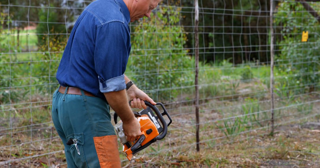 Man Operating Chainsaw Near Fence in Rural Setting - Free Images, Stock Photos and Pictures on Pikwizard.com