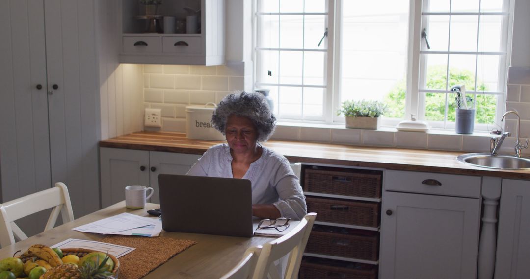 Senior woman working remotely on laptop in cozy kitchen - Free Images, Stock Photos and Pictures on Pikwizard.com