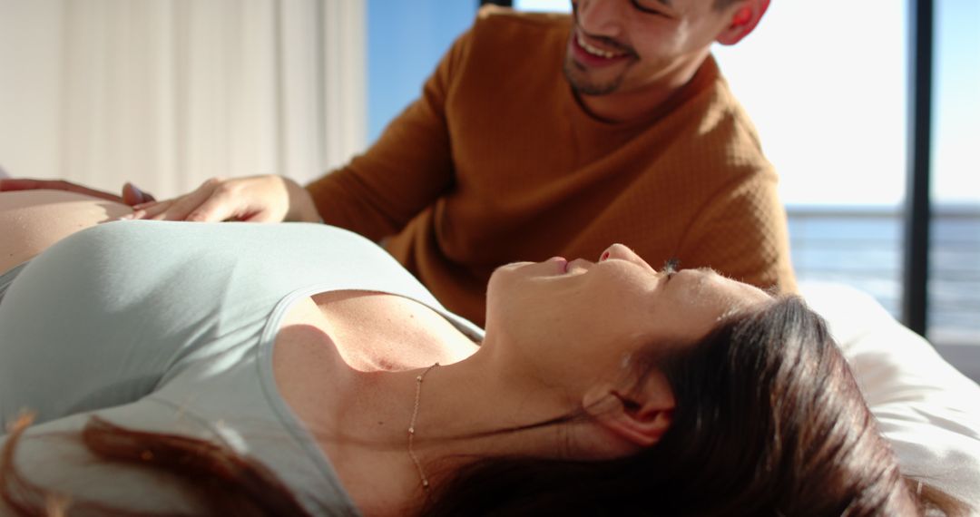 Diverse Partners Enjoying Pregnancy Together in Serene Coastal Bedroom