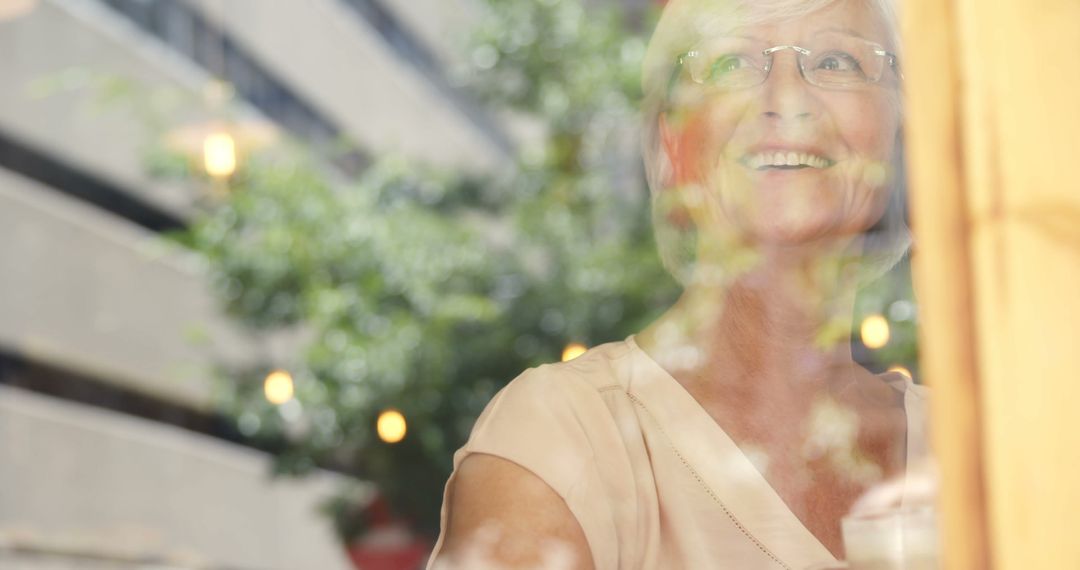 Smiling Elderly Woman Looking Out Window with Reflections of Trees - Free Images, Stock Photos and Pictures on Pikwizard.com