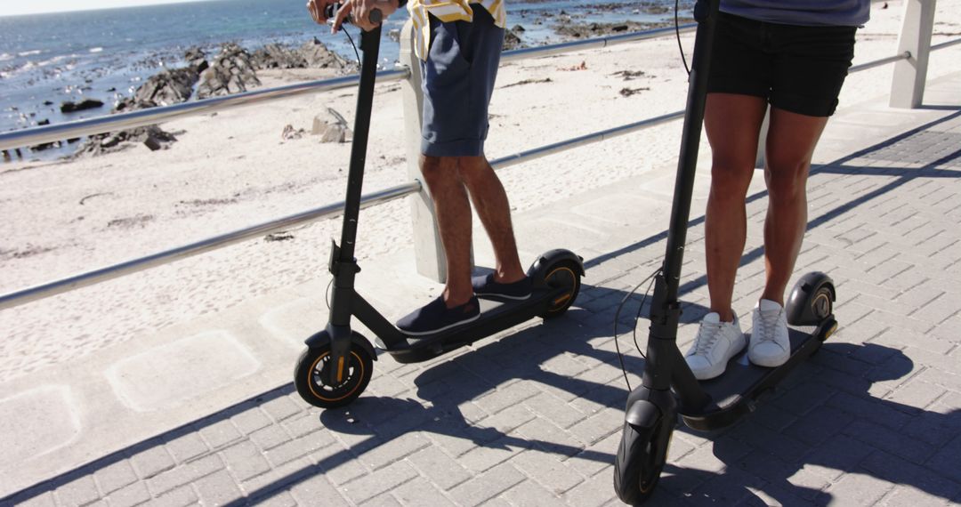 Two People Riding Electric Scooters by Beachfront Promenade - Free Images, Stock Photos and Pictures on Pikwizard.com