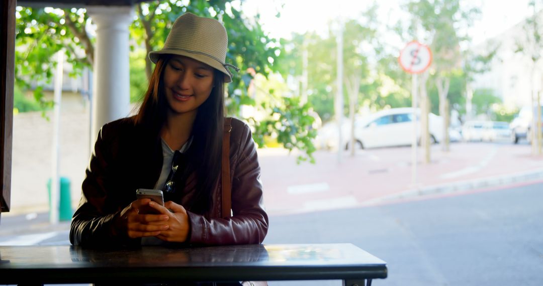 Smiling Young Woman Sitting Outdoors Using Smartphone - Free Images, Stock Photos and Pictures on Pikwizard.com