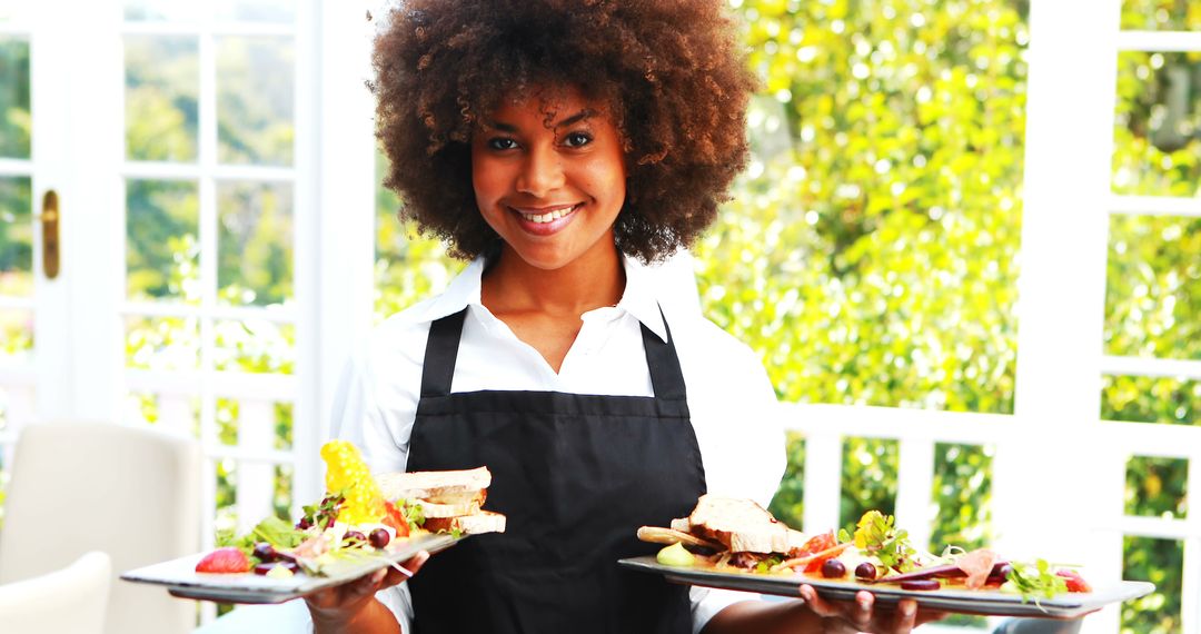 Smiling African American waitress holding plates of delicious food in restaurant - Free Images, Stock Photos and Pictures on Pikwizard.com