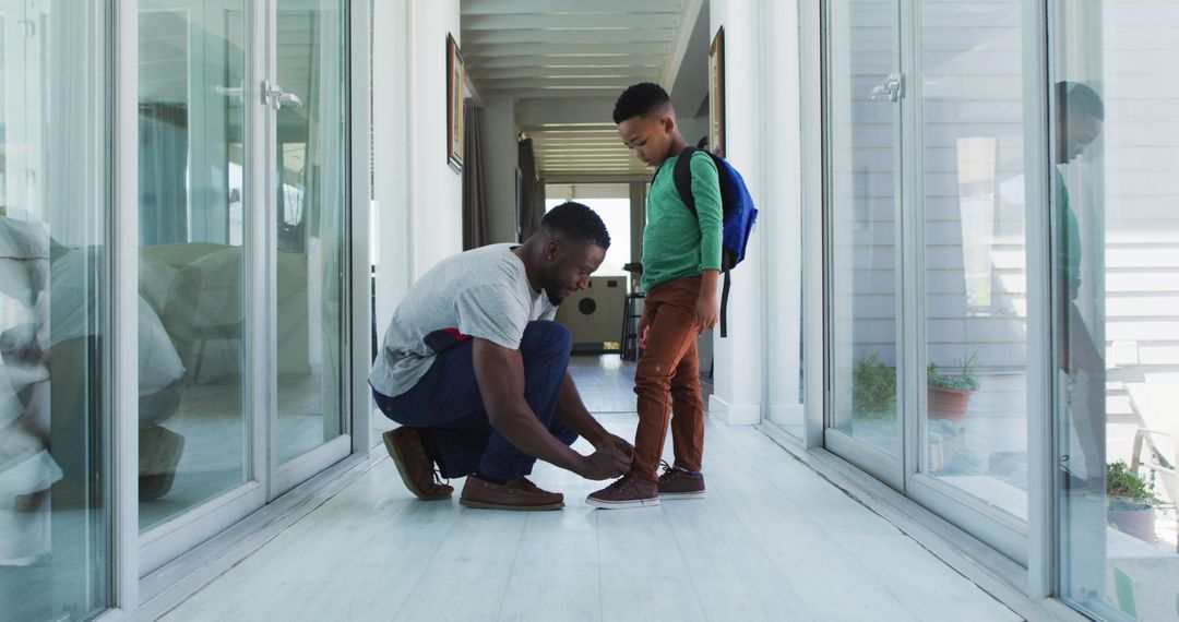 African american father helping his son with tying shoes in hallway - Free Images, Stock Photos and Pictures on Pikwizard.com