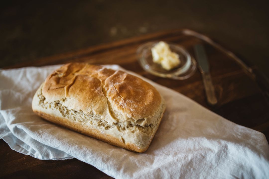 Rustic homemade white bread loaf on linen cloth with butter and knife on wooden board