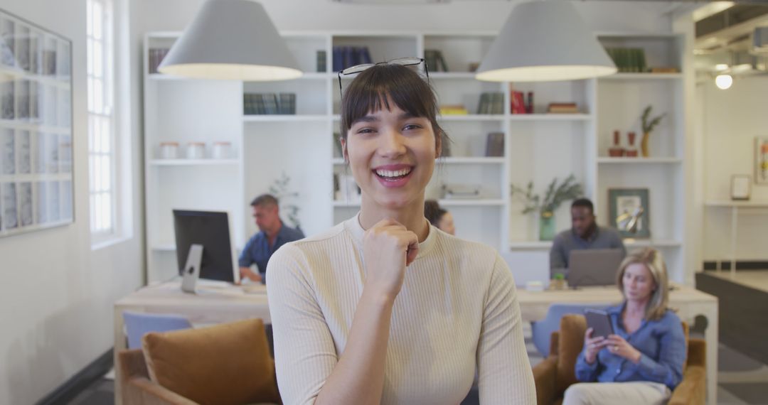 Smiling Young Woman in Modern Office with Colleagues in Background - Free Images, Stock Photos and Pictures on Pikwizard.com