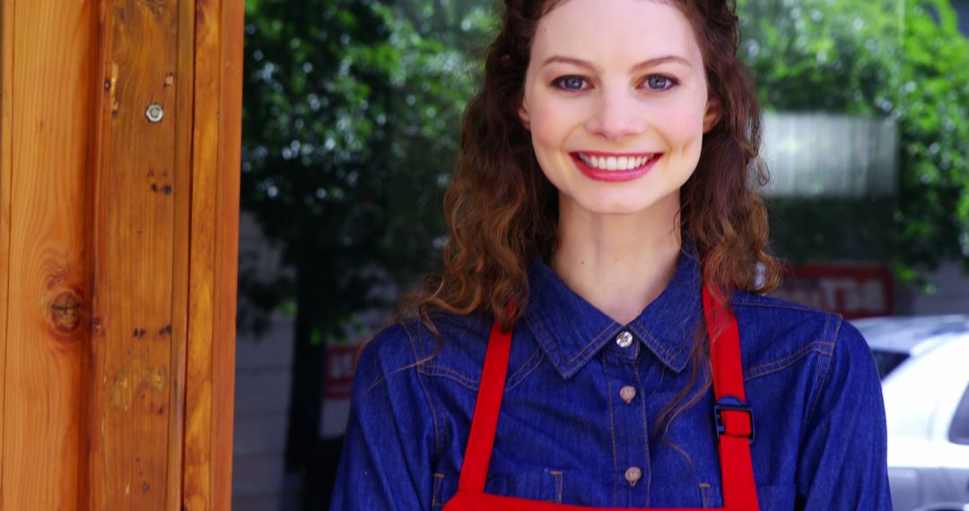 Smiling Cafe Worker Wearing Denim Shirt and Red Apron at Entrance - Free Images, Stock Photos and Pictures on Pikwizard.com