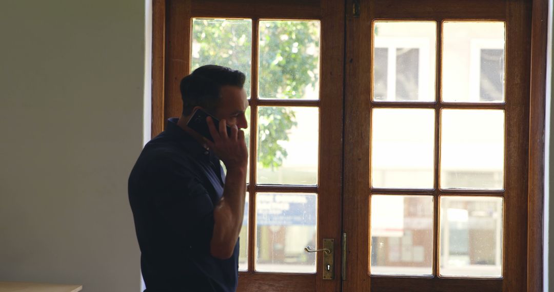 Businessman Standing by Window Talking on Phone - Free Images, Stock Photos and Pictures on Pikwizard.com