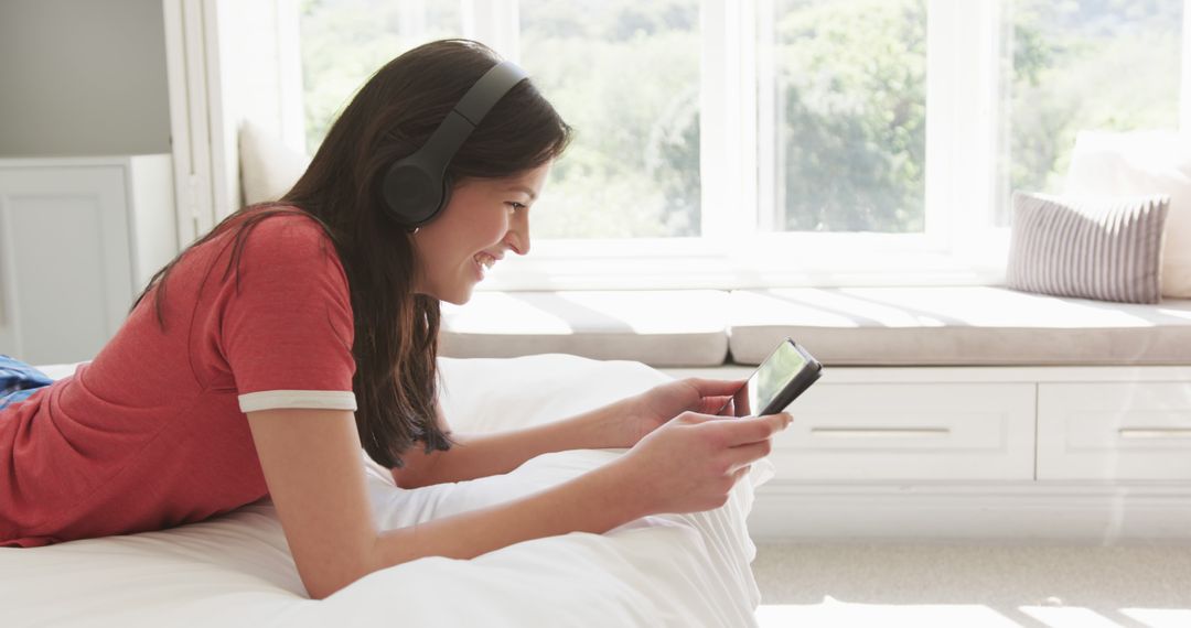 Young Woman Relaxing on Bed with Headphones and Smartphone - Free Images, Stock Photos and Pictures on Pikwizard.com