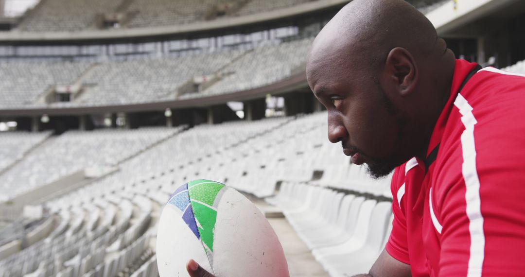 Rugby Player Contemplating with Ball in Empty Stadium