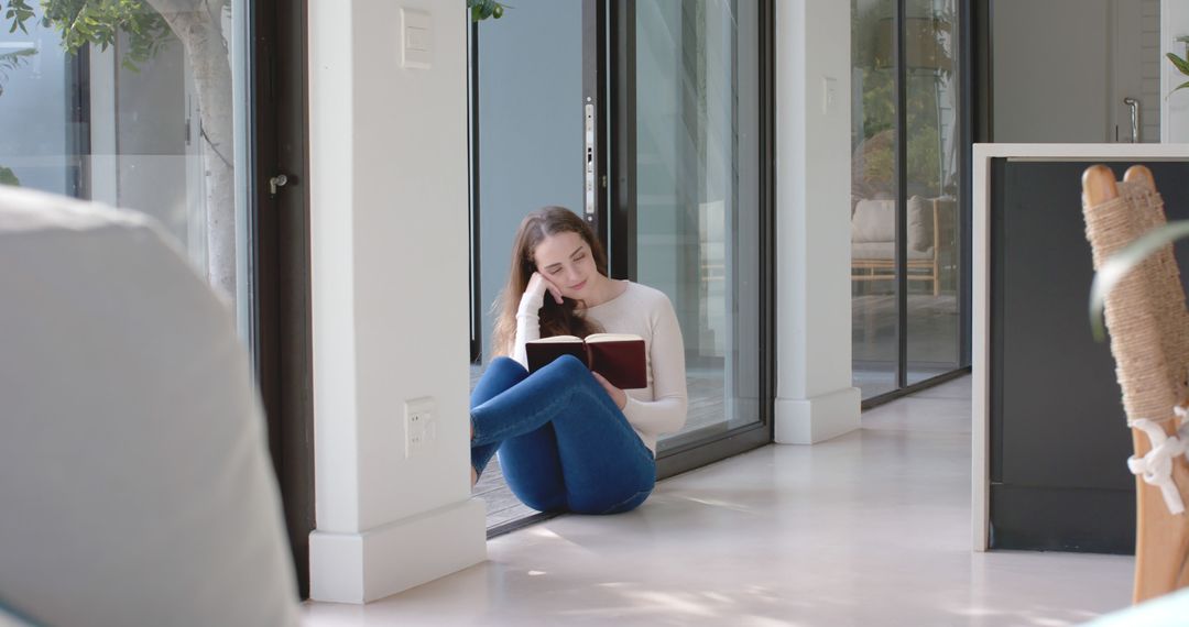 Relaxed Young Woman Reading Book by Sunlit Window at Home - Free Images, Stock Photos and Pictures on Pikwizard.com