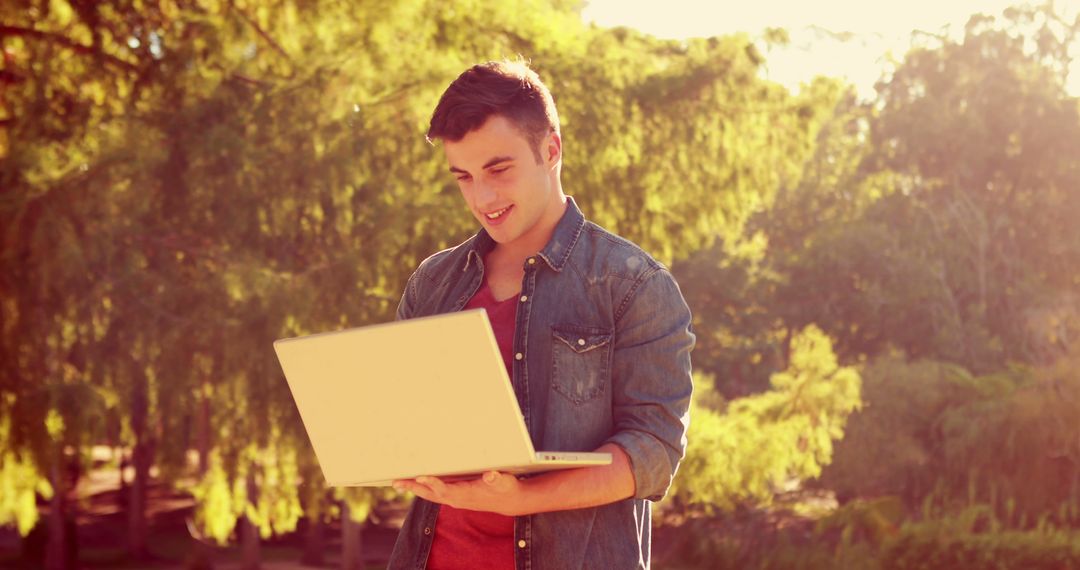 Young Man Smiling While Using Laptop Outdoors - Free Images, Stock Photos and Pictures on Pikwizard.com