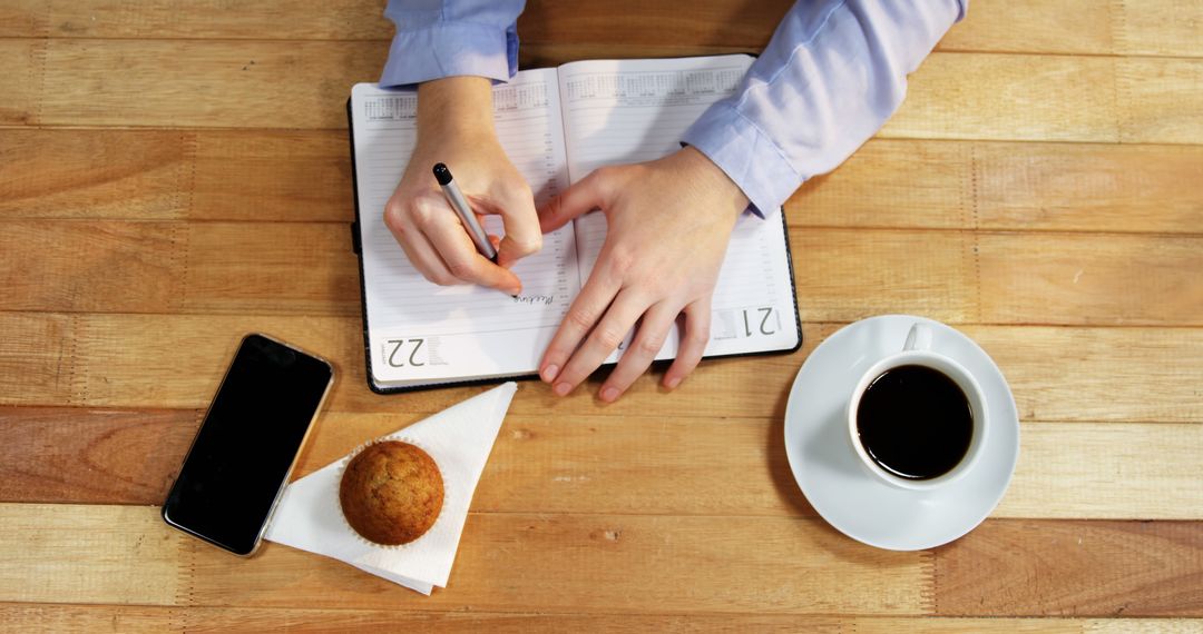 Hands Writing in Planner with Coffee Muffin and Phone on Wooden Table - Free Images, Stock Photos and Pictures on Pikwizard.com