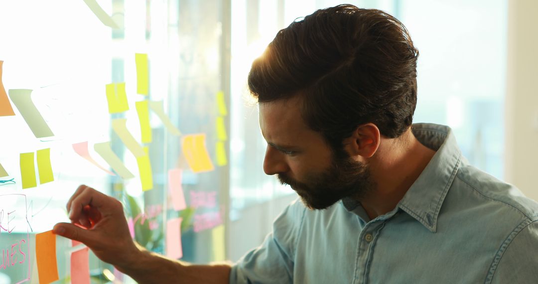 Businessman Brainstorming Ideas on Glass Wall with Sticky Notes - Free Images, Stock Photos and Pictures on Pikwizard.com