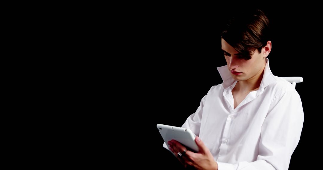 Focused Young Man Reading on Tablet in Dark Background - Free Images, Stock Photos and Pictures on Pikwizard.com