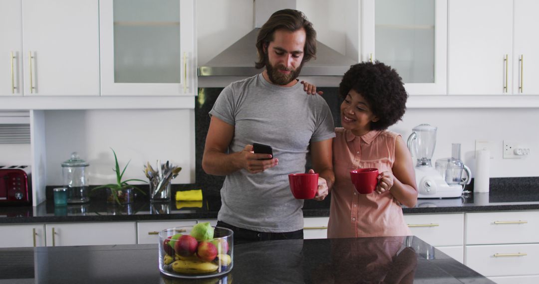 Biracial couple holding coffee cup using smartphone in the kitchen at home - Free Images, Stock Photos and Pictures on Pikwizard.com