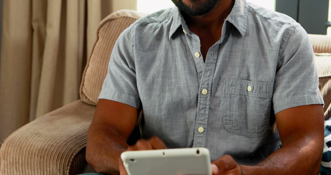 Relaxed Man Using Digital Tablet at Home in Casual Shirt - Free Images, Stock Photos and Pictures on Pikwizard.com