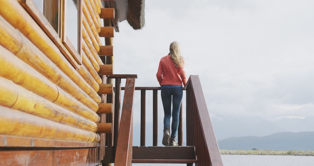 Woman Standing on Wooden Staircase of Log Cabin Overlooking Lake - Free Images, Stock Photos and Pictures on Pikwizard.com