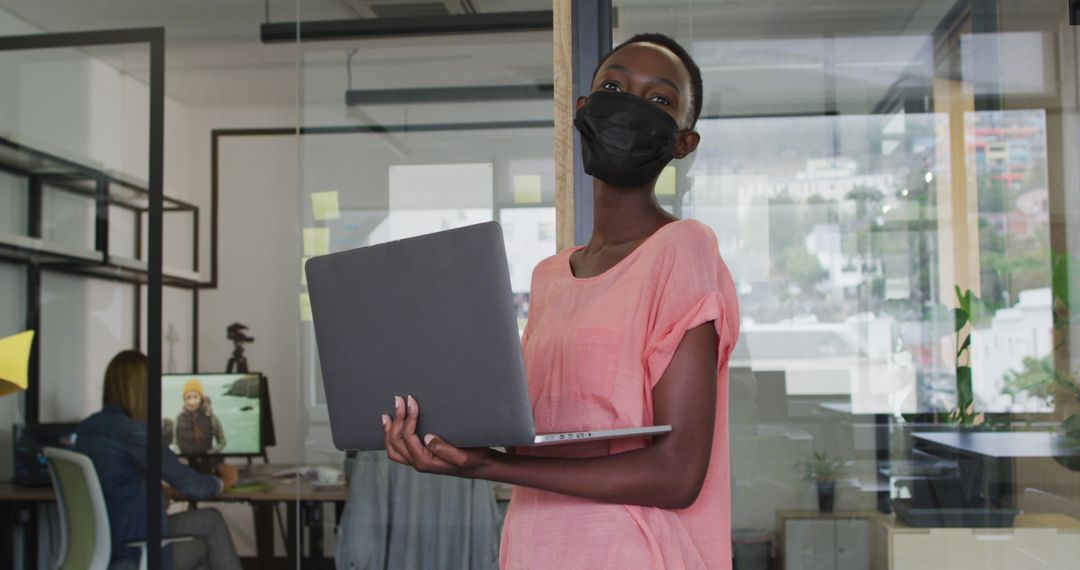 Confident Businesswoman Wearing Mask Holding Laptop in Modern Office - Free Images, Stock Photos and Pictures on Pikwizard.com