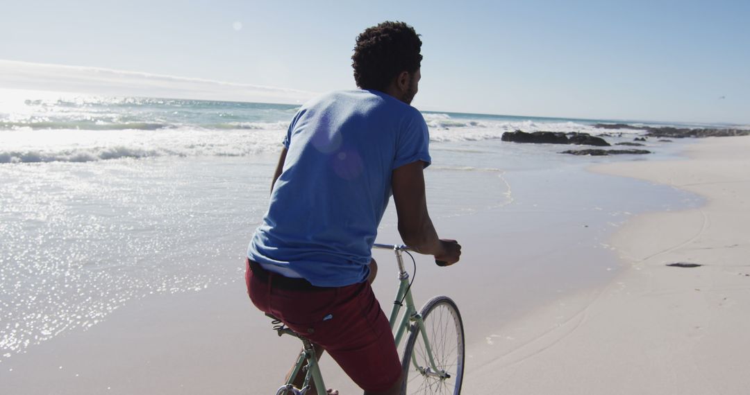 African american man smiling and riding bike on the beach - Free Images, Stock Photos and Pictures on Pikwizard.com