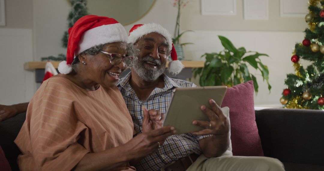 Smiling Senior Couple in Santa Hats Using Tablet at Christmas