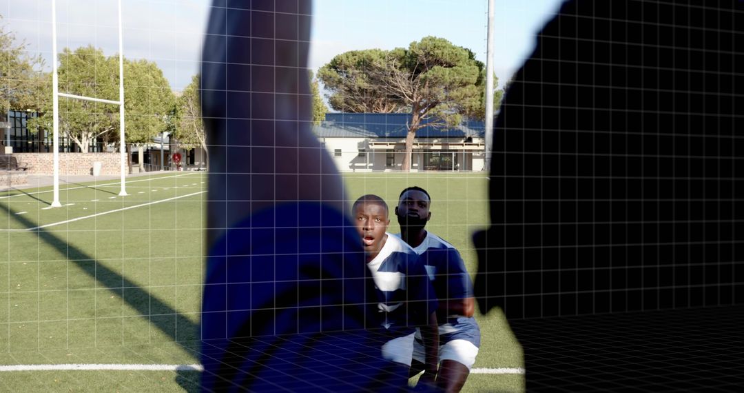 Kneeling rugby players reacting toward camera while silhouetted teammate blocking foreground on fiel