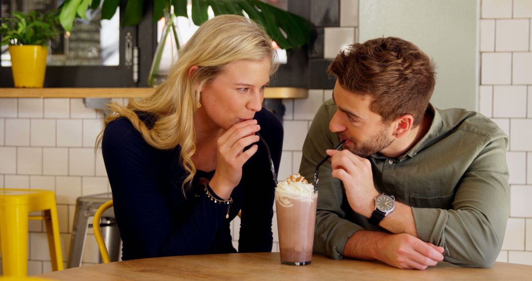 A young Caucasian couple enjoys a milkshake together, sharing a straw in a cozy cafe setting - Free Images, Stock Photos and Pictures on Pikwizard.com