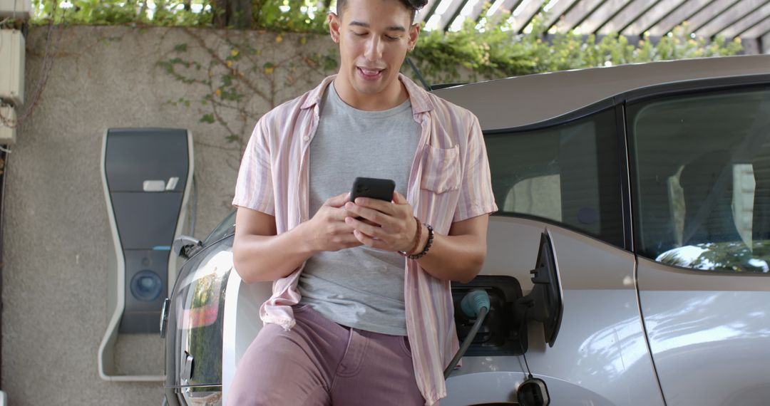 Man Using Smartphone While Charging Electric Car at Home Station