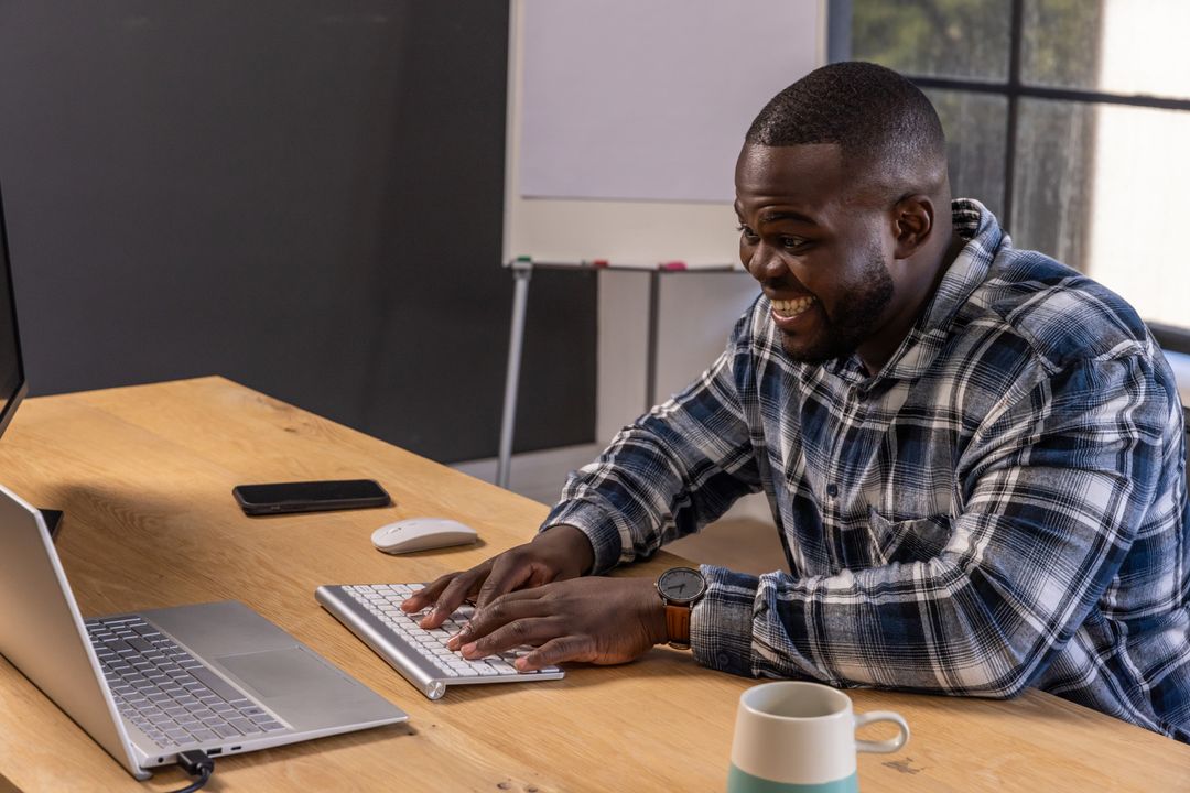 Smiling Man Typing on Laptop at Modern Office Workstation