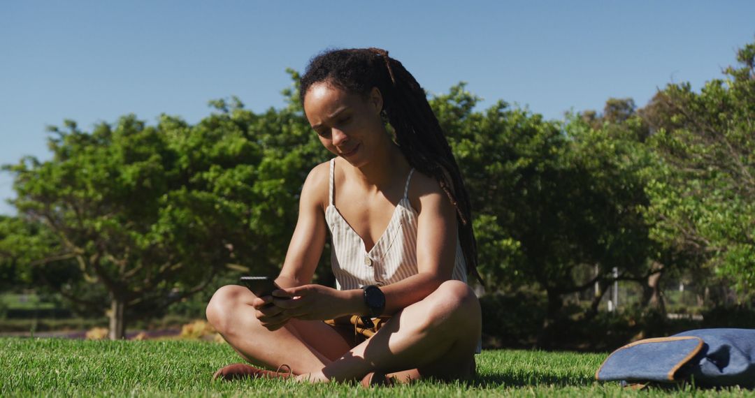 Young woman relaxing in park with mobile phone on sunny day - Free Images, Stock Photos and Pictures on Pikwizard.com