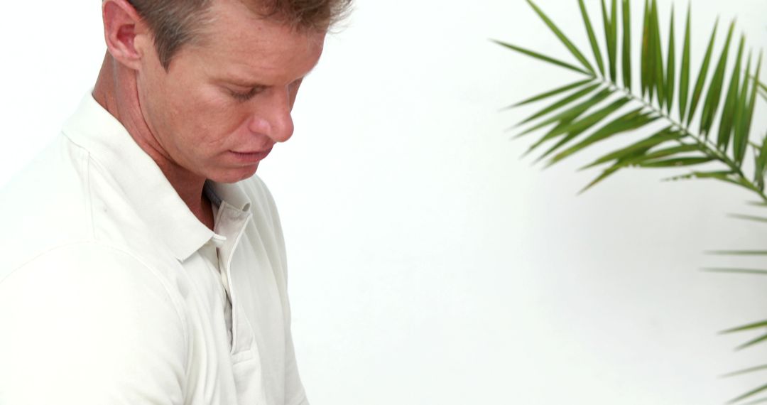 Man in White Polo Shirt Looking Down with Green Palm Leaf Background - Free Images, Stock Photos and Pictures on Pikwizard.com