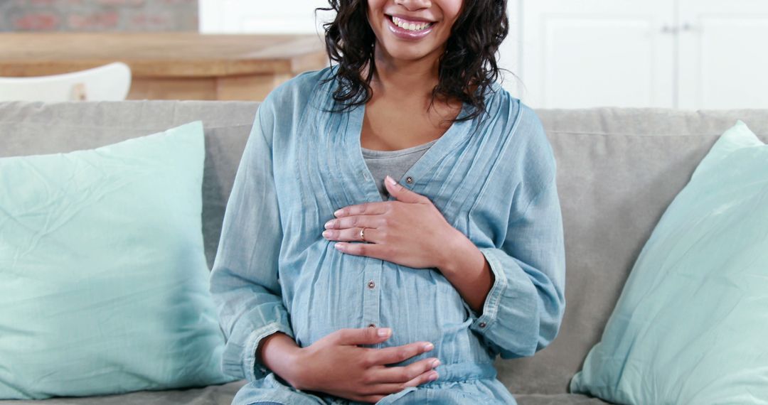 Smiling Pregnant Woman Sitting on Sofa with Hands on Belly - Free Images, Stock Photos and Pictures on Pikwizard.com