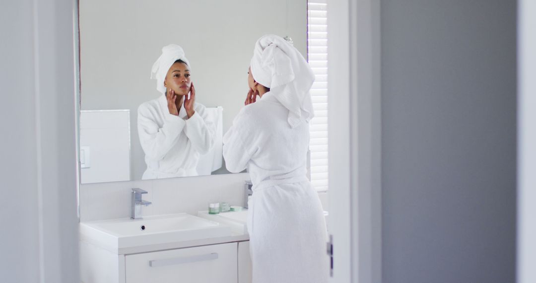 Woman examining face in bathroom mirror wearing bathrobe and towel - Free Images, Stock Photos and Pictures on Pikwizard.com