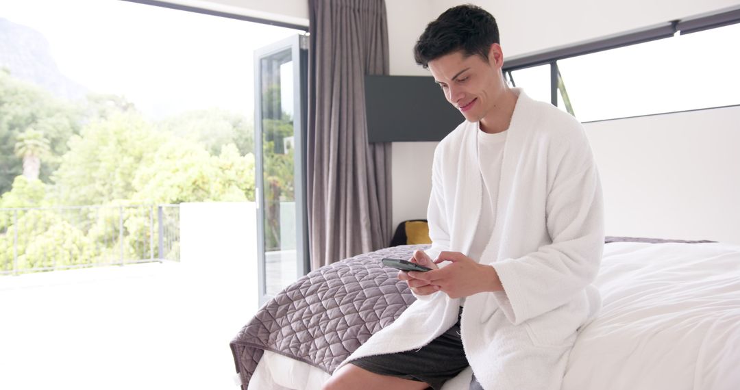 Relaxed Man Sitting on Bed Using Smartphone