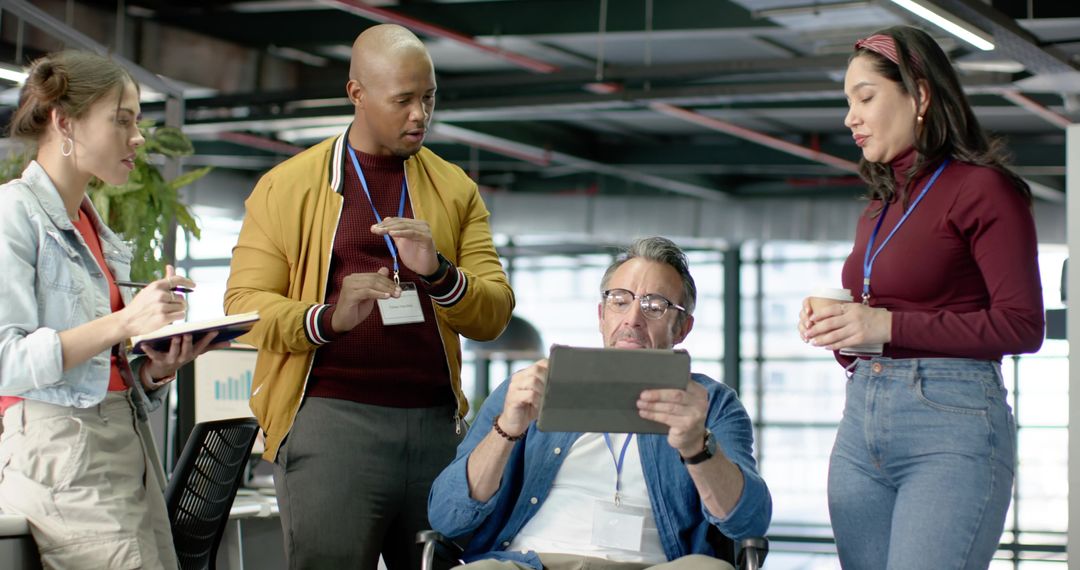 Diverse team collaborating around tablet in modern open-plan office during meeting